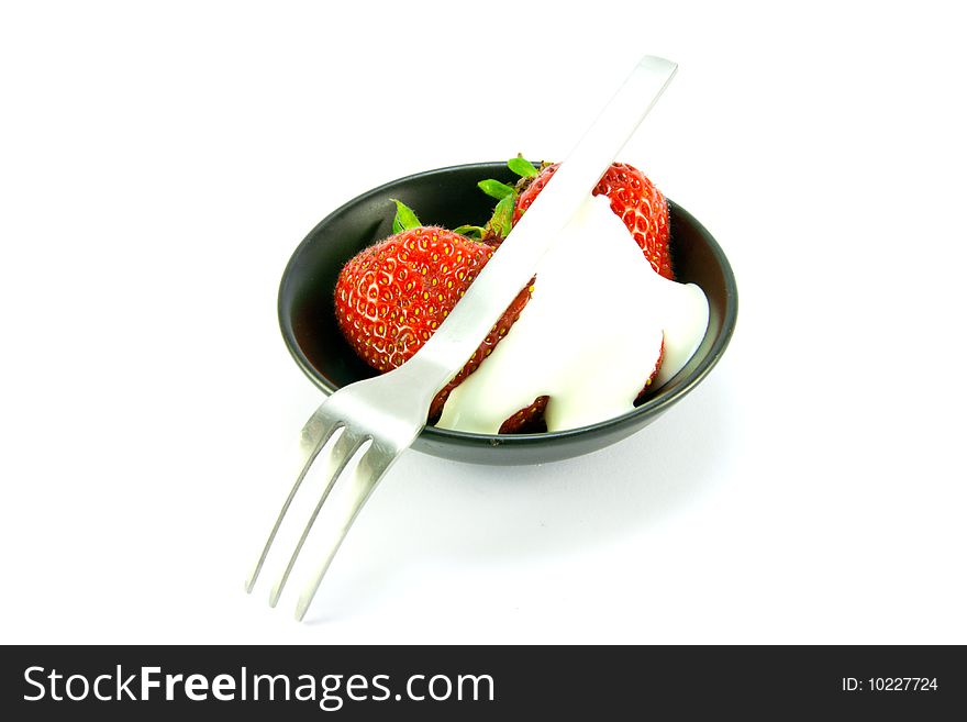 Sliced and whole red fresh strawberries with cream and small fork in a small black dish on a white background. Sliced and whole red fresh strawberries with cream and small fork in a small black dish on a white background