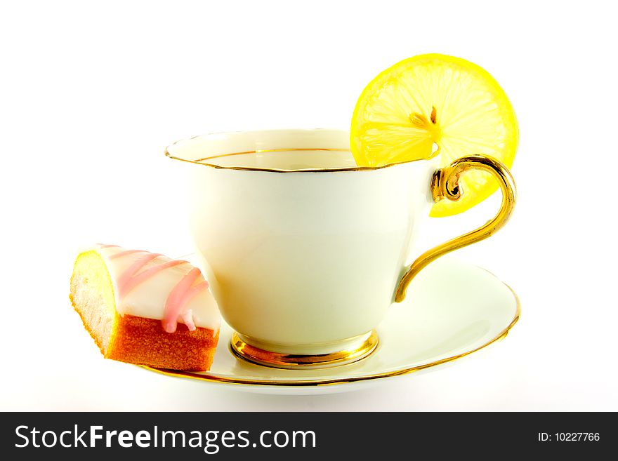 Tea in a cup and saucer with pink slice of cake and a slice of lemon on a white background. Tea in a cup and saucer with pink slice of cake and a slice of lemon on a white background