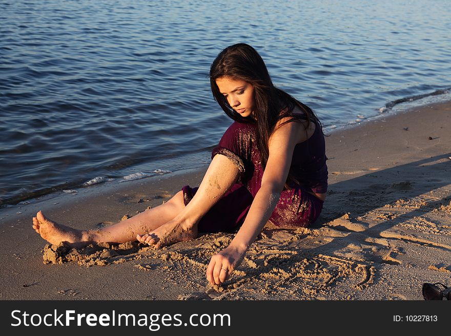 Beautiful girl playing in sand on beach at sunset. Beautiful girl playing in sand on beach at sunset
