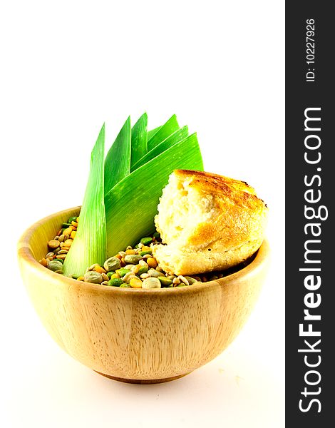 Wooden bowl of soup pulses with leek and crusty bread on a white background