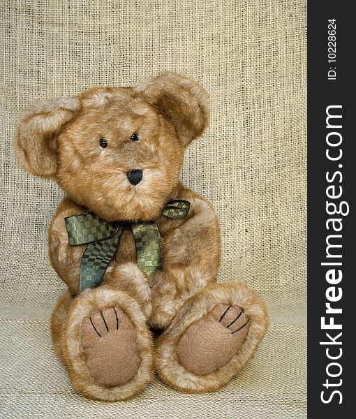 A cute little brown toy stuffed bear with a green bow, vertical with copy space