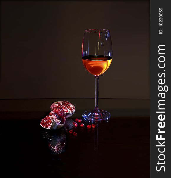 Glass with White wine and red pomegranate with reflection on dark background