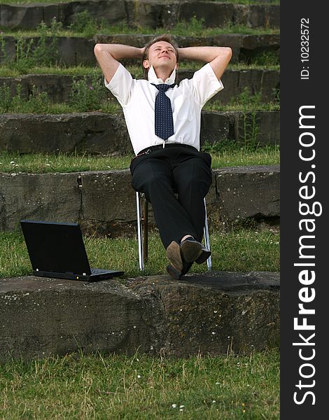 Relaxing businessman sitting outdoor with laptop