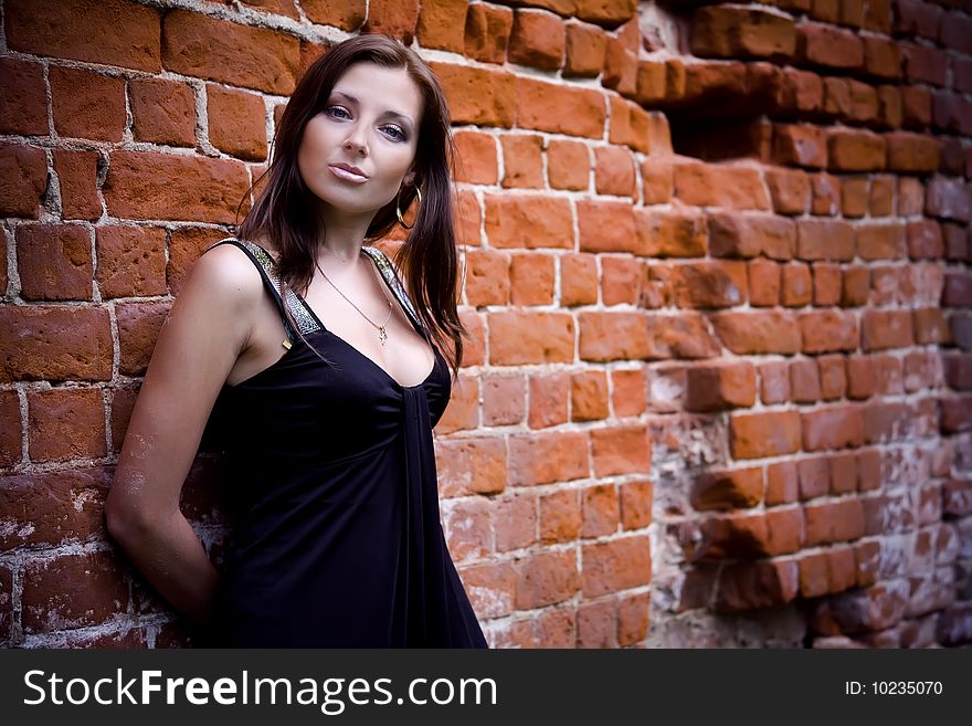 Charming woman in black dress near red brick wall. Charming woman in black dress near red brick wall