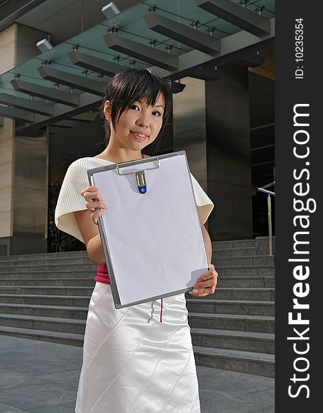 Beautiful young and modern Asian woman in the city showing a clipboard.