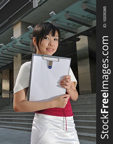 Beautiful young and modern Asian woman in the city showing a clipboard. Beautiful young and modern Asian woman in the city showing a clipboard.