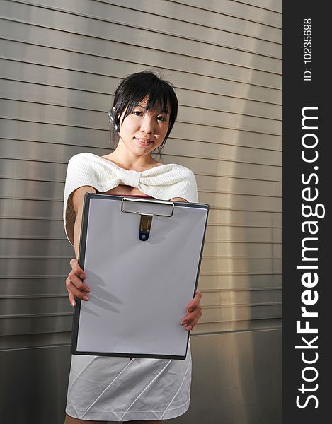 Beautiful young and modern Asian woman in the city showing a clipboard. Beautiful young and modern Asian woman in the city showing a clipboard.