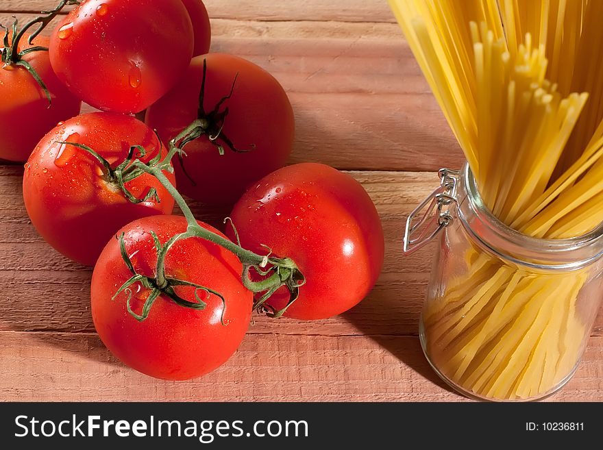 Fresh tomatoes in front of a container with raw spaghetti