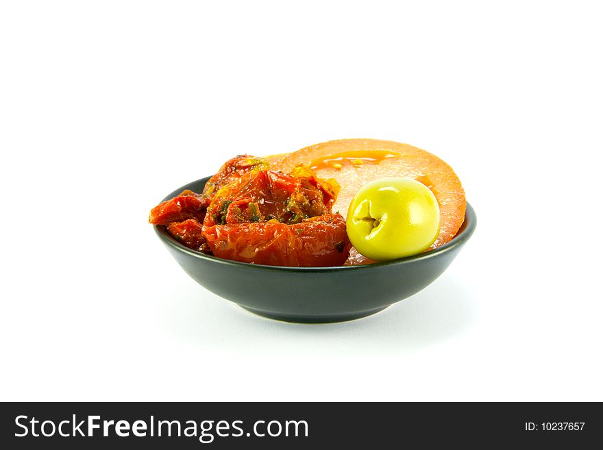 Sun dried tomatoes, slices of tomatoes and a green olive in a small black bowl on a white background. Sun dried tomatoes, slices of tomatoes and a green olive in a small black bowl on a white background