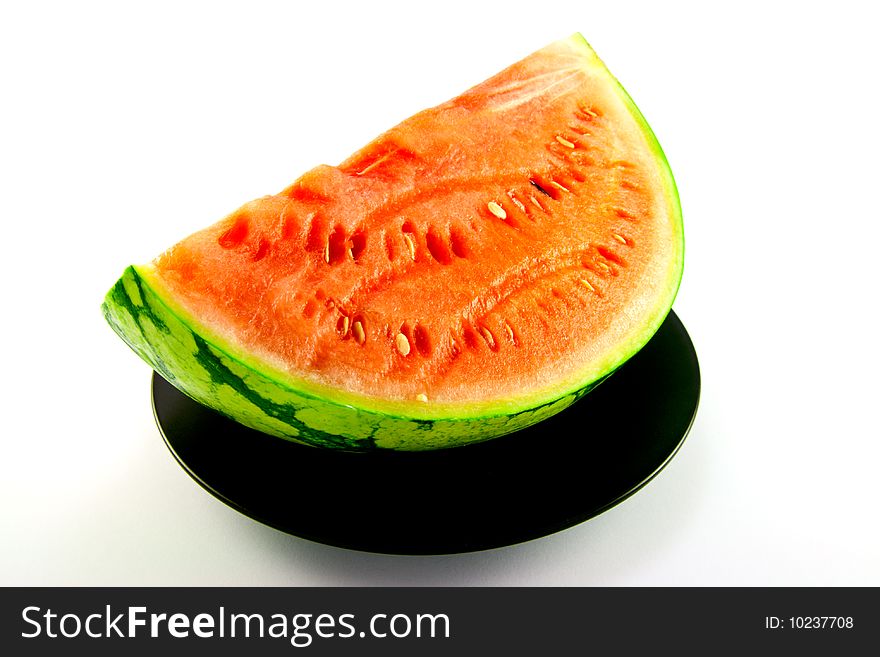 Slice of watermelon with green skin and red melon with seeds on a black plate with a white background. Slice of watermelon with green skin and red melon with seeds on a black plate with a white background