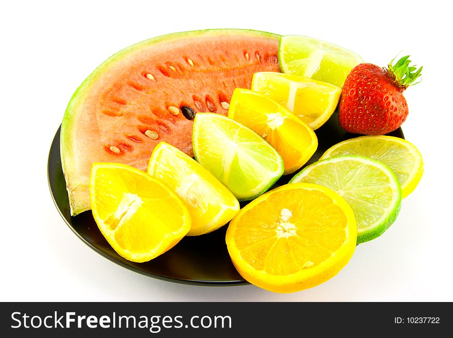 Slice of watermelon with lemon, lime and orange segments and single red strawberry on a black plate with a white background. Slice of watermelon with lemon, lime and orange segments and single red strawberry on a black plate with a white background