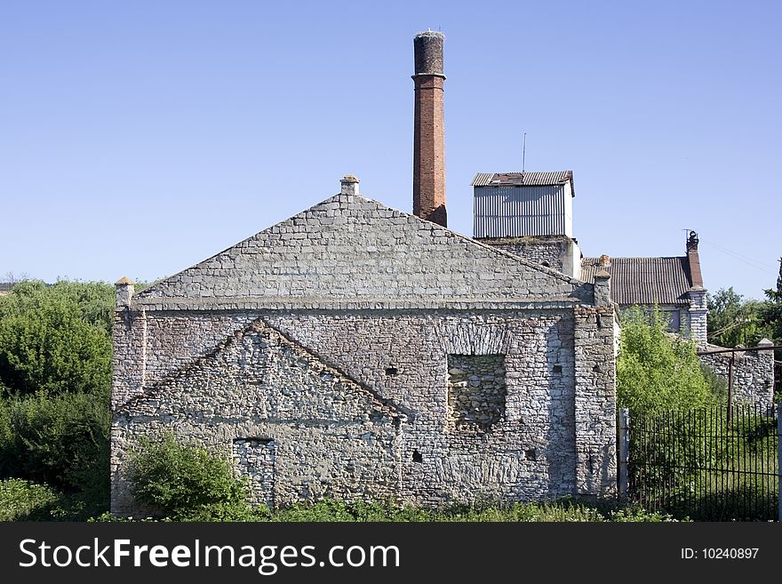An abandoned building of an old 19th century factory with a long brick smokestack tower. An abandoned building of an old 19th century factory with a long brick smokestack tower.