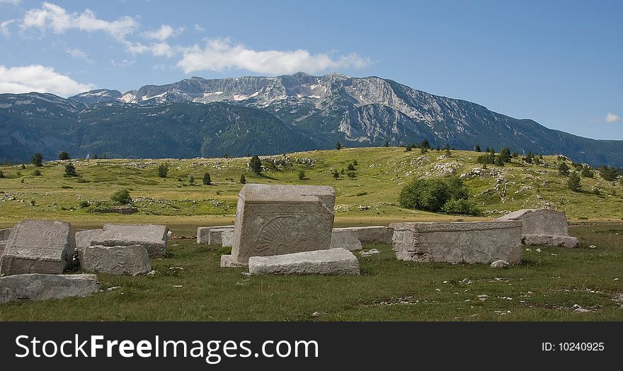 Old medieval monuments, made from white marble, and mountain rising in the background, cloudy sky, summertime.