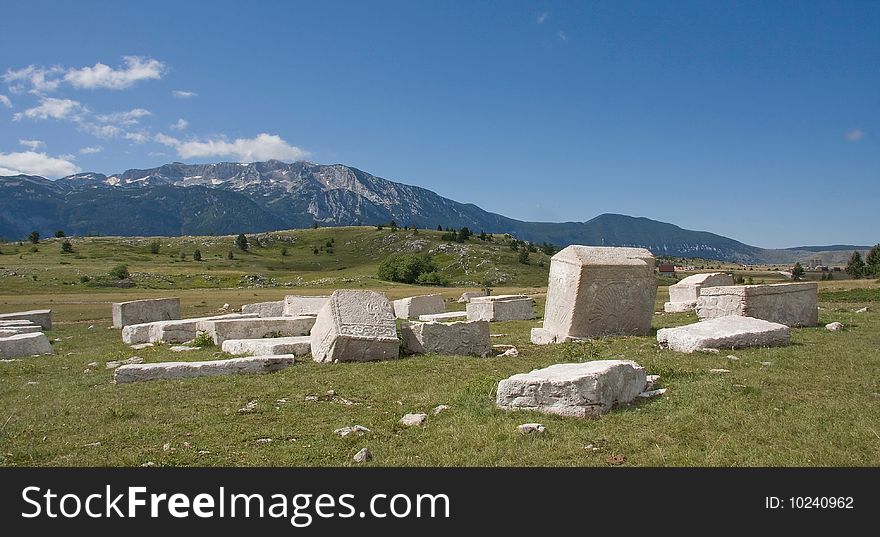 Old medieval monuments, made from white marble, and mountain rising in the background, cloudy sky, summertime.