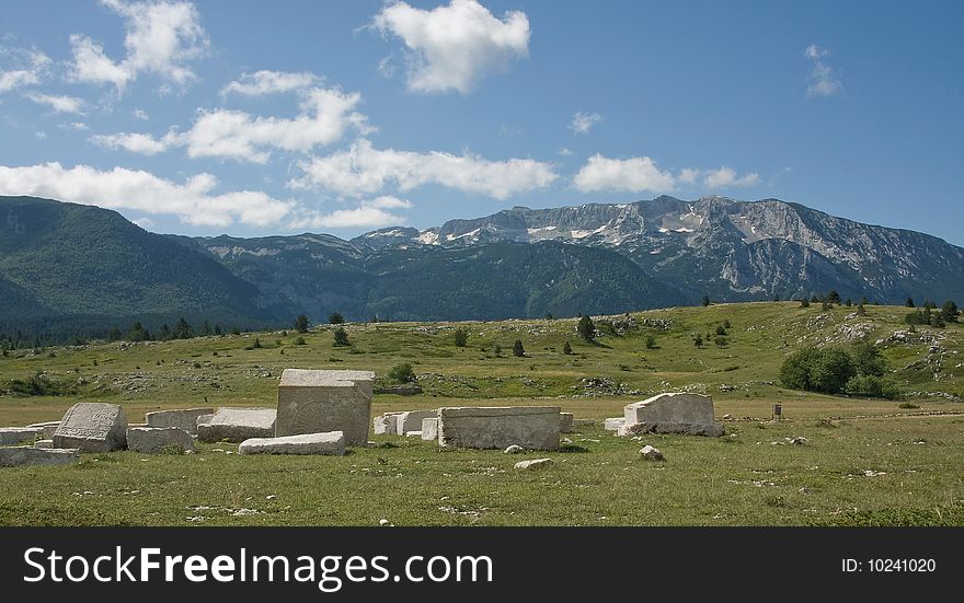 Old medieval monuments, made from white marble, and mountain rising in the background, cloudy sky, summertime.