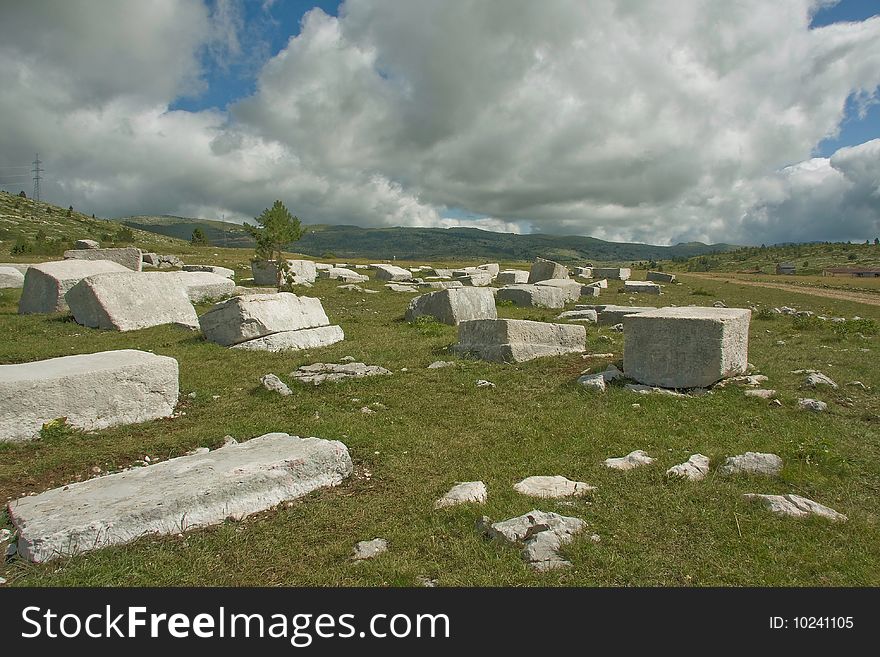 Old medieval monuments, made from white marble, and mountain rising in the background, cloudy sky, summertime.