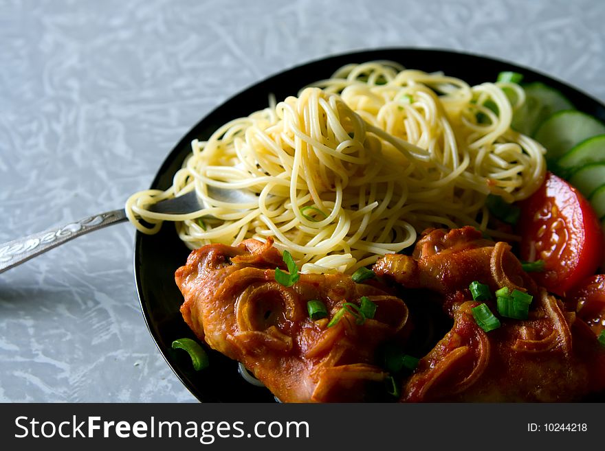 A plate with chicken wings, spaghetti and pieces of tomatoes and cucumbers. A plate with chicken wings, spaghetti and pieces of tomatoes and cucumbers