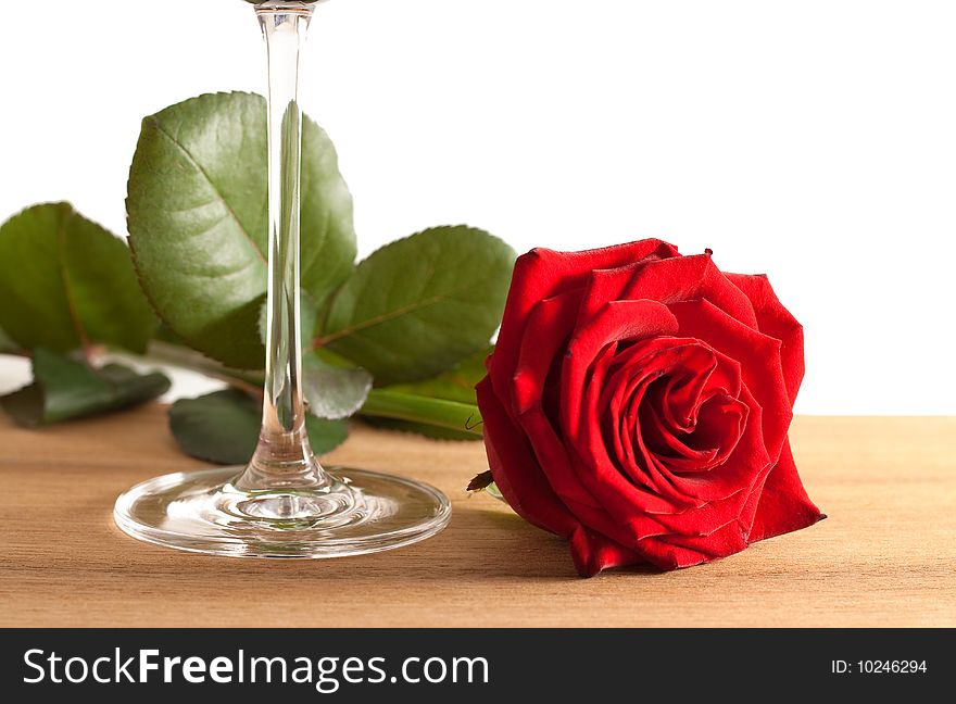 A red rose and a wine glass on a wooden bottom isolated on white background. A red rose and a wine glass on a wooden bottom isolated on white background