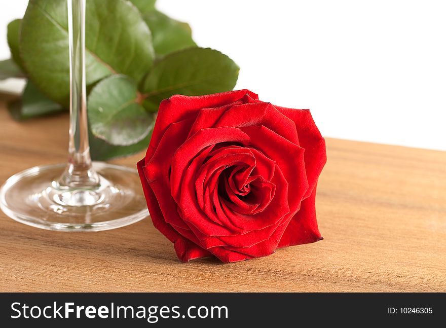 A red rose and a wine glass on a wooden bottom isolated on white background. A red rose and a wine glass on a wooden bottom isolated on white background