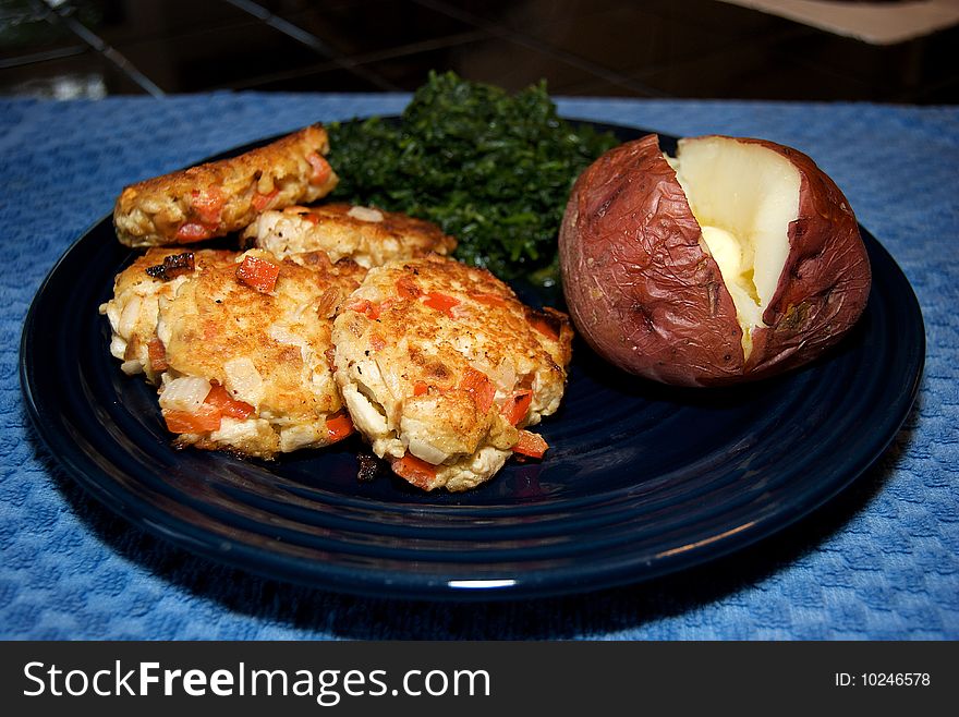 Crab cakes plated with a red potato and spinach. Crab cakes plated with a red potato and spinach.