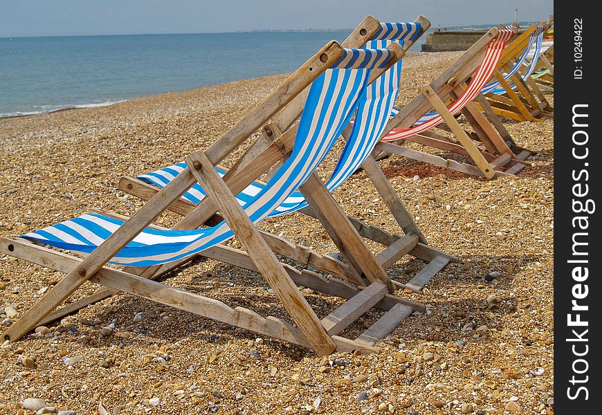 Row of striped deckchairs lined up on Brighton beach awaiting sunbathers. Row of striped deckchairs lined up on Brighton beach awaiting sunbathers.