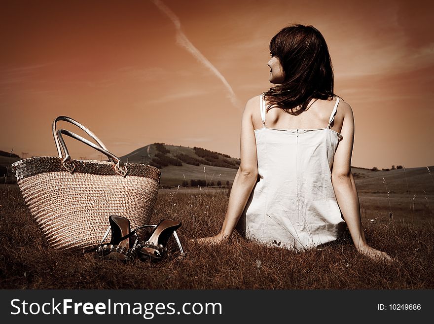 Woman sit on grass with bag and shoes