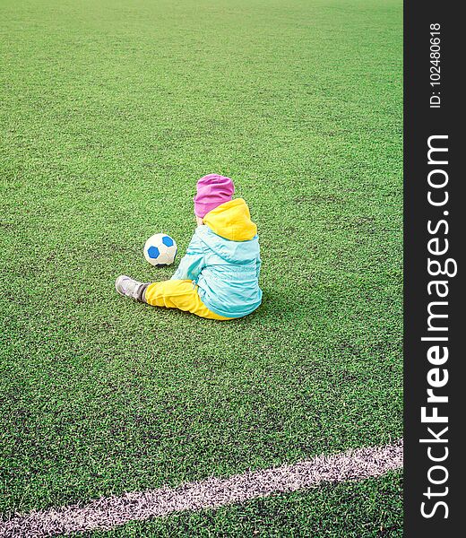 Little girl child on football field, in sportswear, training, plays with soccerball on artificial lawn