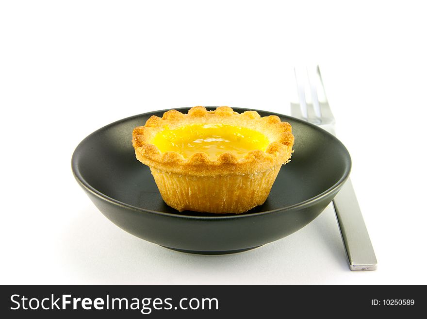 Single small yellow lemon jam tart in a small black dish with a fork on a white background