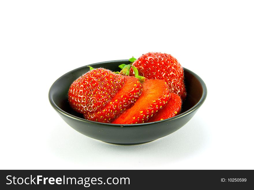 Sliced and whole red fresh strawberries in a small black dish on a white background