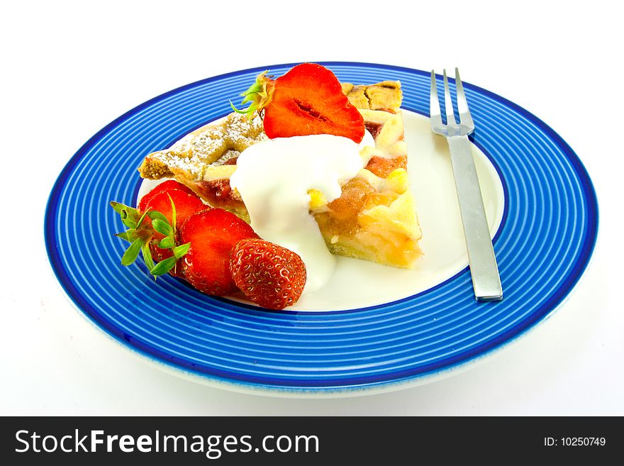 Slice of apple and strawberry pie with strawberries, cream and a fork on a blue plate with a white background. Slice of apple and strawberry pie with strawberries, cream and a fork on a blue plate with a white background