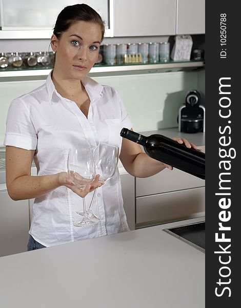 Young attractive woman pouring out wine in kitchen