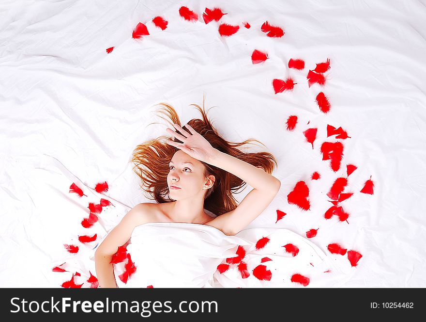 Beautiful girl in bed with red plumage