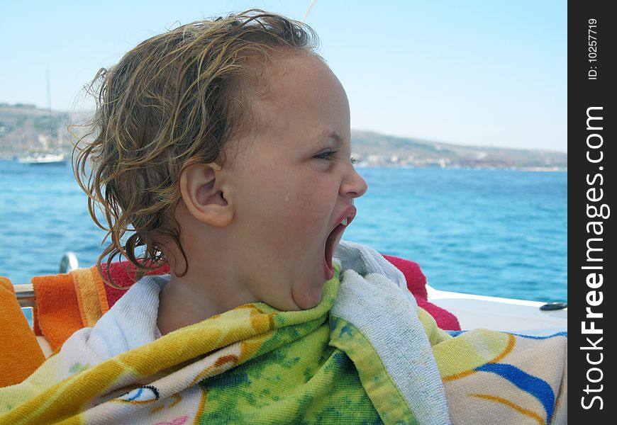 A young toddler sitting on a boat in the middle of the sea wrapped in a towel and yawning. A young toddler sitting on a boat in the middle of the sea wrapped in a towel and yawning