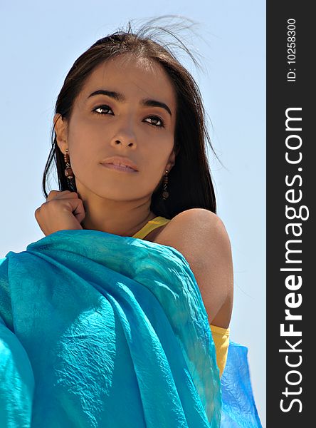 Young Hispanic woman with a blue scarf against a blue sky. Young Hispanic woman with a blue scarf against a blue sky.