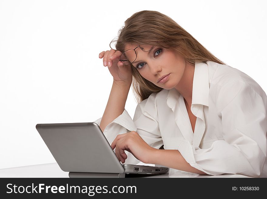 The modern young woman sits at a table with the personal computer, holds points in a hand and looks in the chamber. The modern young woman sits at a table with the personal computer, holds points in a hand and looks in the chamber