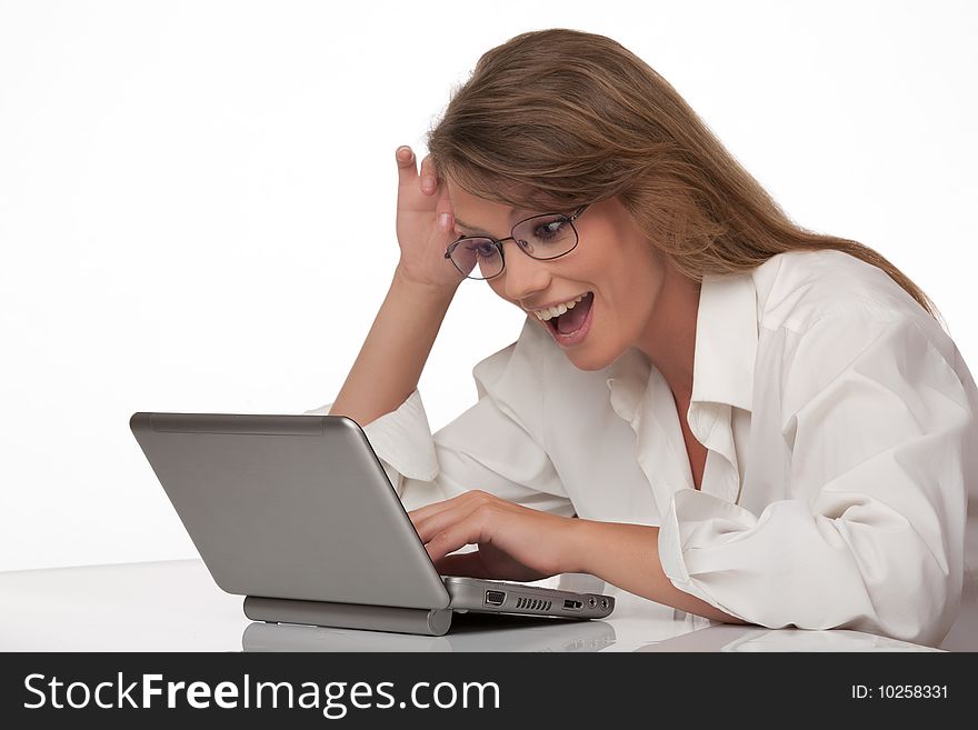 The modern young woman sits at a table with a personal computer, joyfully smiling, looks at the screen of a computer. The modern young woman sits at a table with a personal computer, joyfully smiling, looks at the screen of a computer