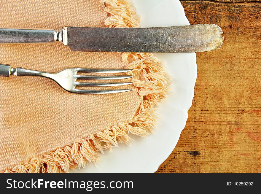 White plate with fork and knife on a rustic wooden table. White plate with fork and knife on a rustic wooden table.