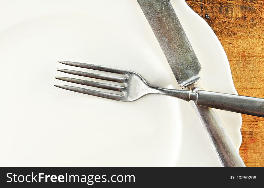 White plate with fork and knife on a rustic wooden table. White plate with fork and knife on a rustic wooden table.