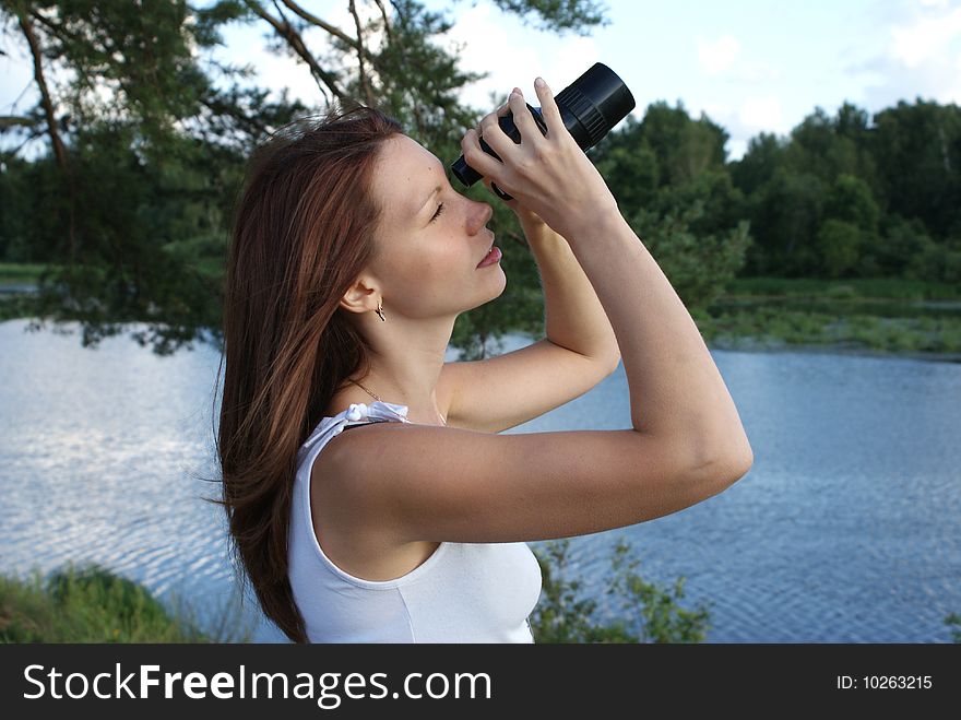 Girl with binoculars on the riverside. It looks in distance.