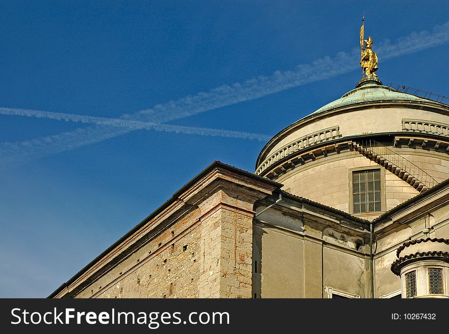 Old building with a golden statue on top and sky with flight trails in the background. Old building with a golden statue on top and sky with flight trails in the background