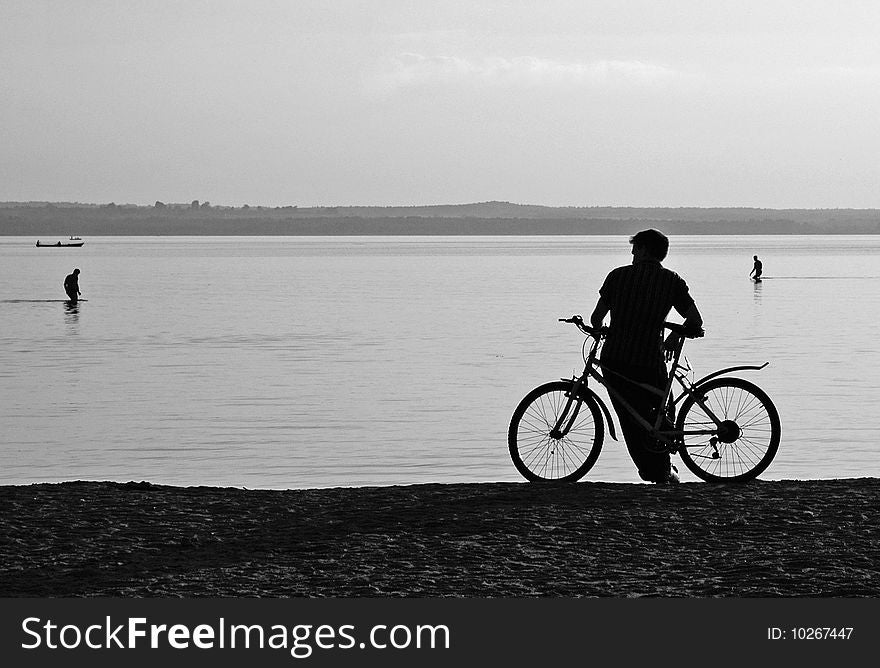 Cyclist on the shore of the lake at sunset. Bathers in the background. Cyclist on the shore of the lake at sunset. Bathers in the background.