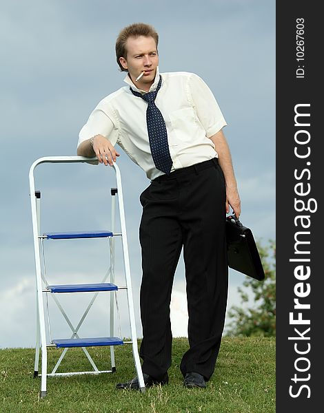 Smoking businessman with ladder and bag outdoor. Smoking businessman with ladder and bag outdoor