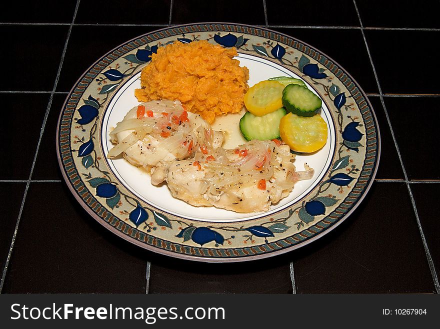 Chicken, mashed sweet potatoes and summer squash and zucchini, plated on a black tile table. Chicken, mashed sweet potatoes and summer squash and zucchini, plated on a black tile table.