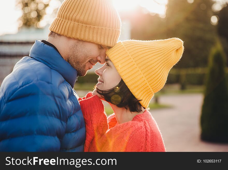 Romantic young couple look at each other with great love, have nice relationship, going to kiss, have walk outdoor in park, wear warm clothes. Lovely couple with eyes full of love and smile.