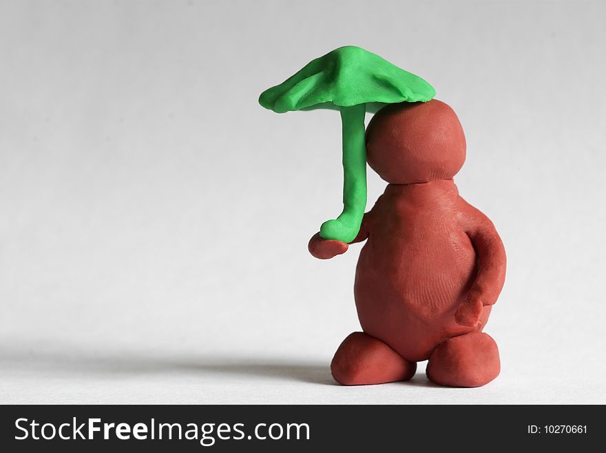 Plasticine man under the green umbrella over grey background