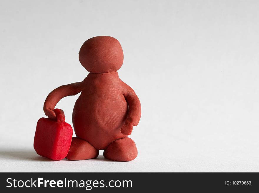 Plasticine man with a red suitcase over grey background