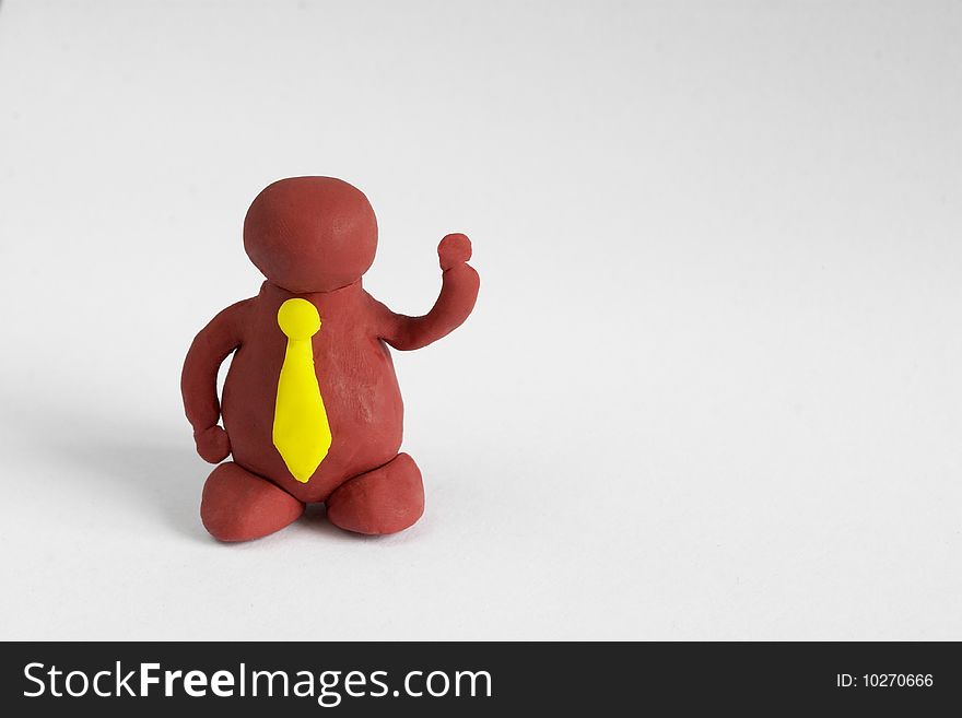 Plasticine man with a yellow tie keeping one hand up over grey background