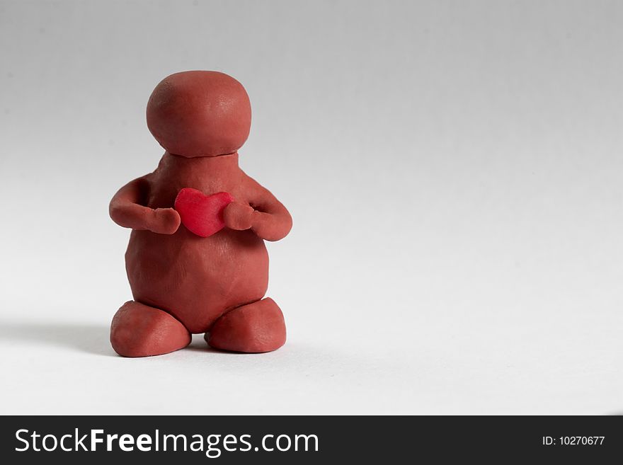 Plasticine man keeping a heart in the hands over grey background