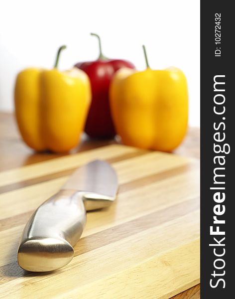 Knife on chopping board and capsicum chilli peppers in the background