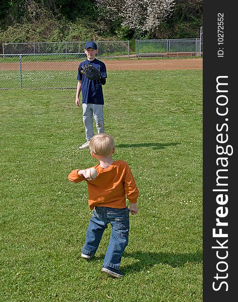 A 3 year old boy wearing orange shirt and blue jeans is throwing a baseball to his big brother between little league game. A 3 year old boy wearing orange shirt and blue jeans is throwing a baseball to his big brother between little league game.